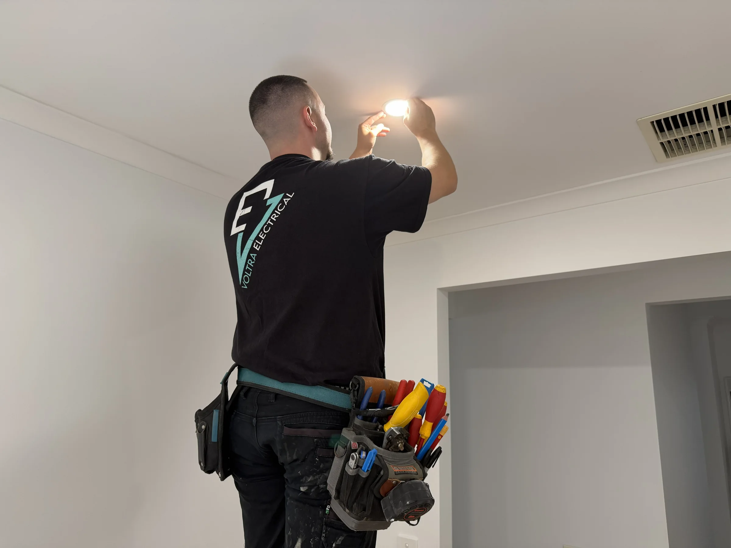 Voltra electrician fitting a ceiling downlight in a home